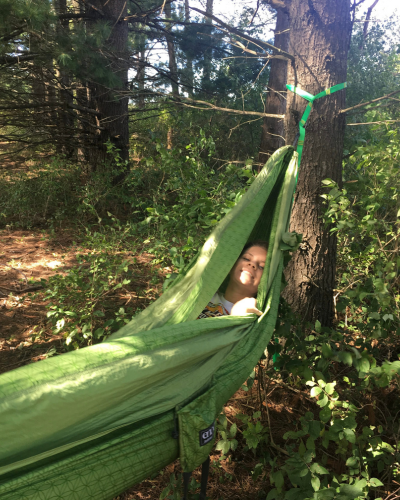 A woman smiles as she snuggles into a green hammock in a forest.