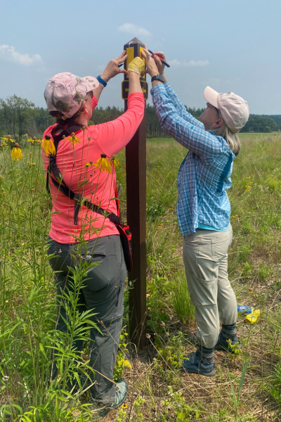 Two volunteers trace plastic yellow blazes to use as an outline for painting them on a wooden post.