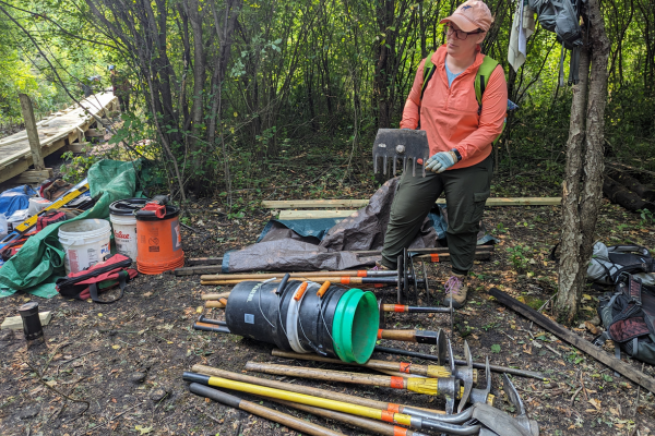 A volunteer stands over a pile of Trailbuilding tools.