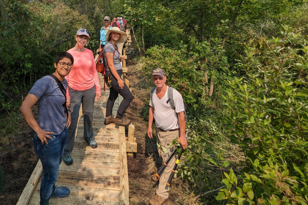 A group of volunteers and Alliance staff members stand a smile on a newly built boardwalk.