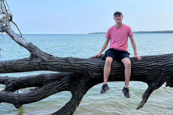 A man sits on a large tree stump over a lake.